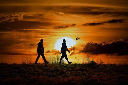 A picture of two people walking in the sunset