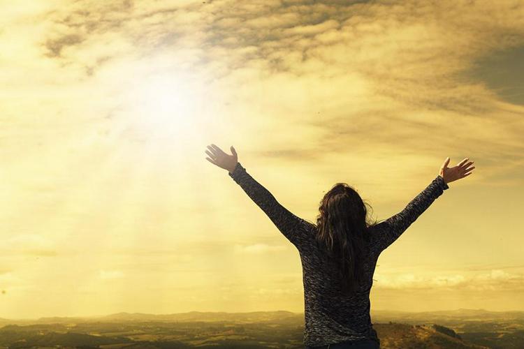 A picture of a woman opening her hands to the sun