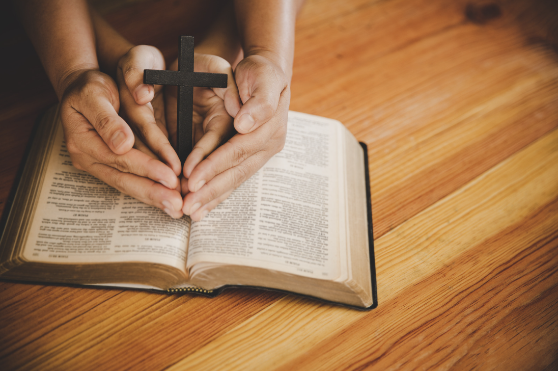 Two hands holding a cross on an open Bible
