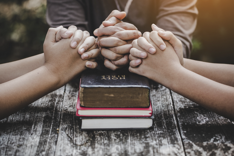 Three pairs of praying hands placed on a Holy Bible