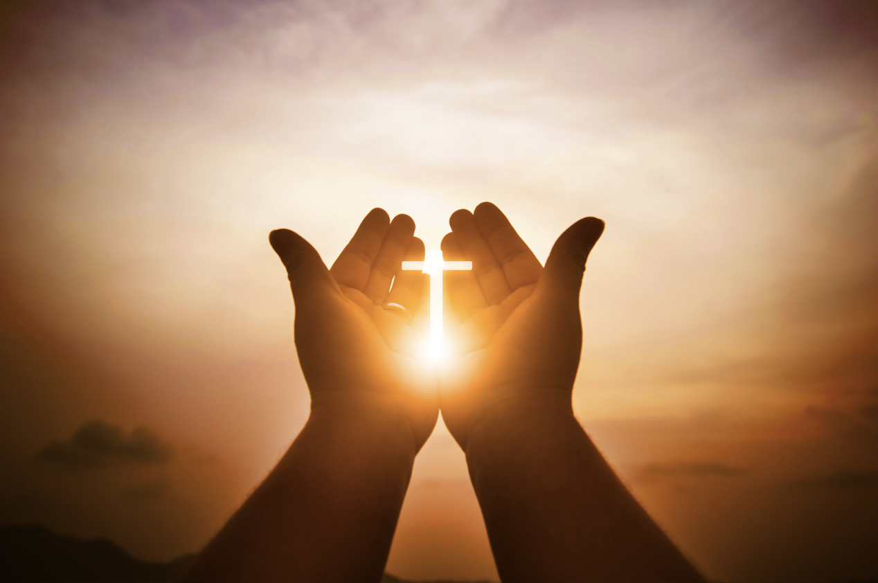 A picture of a person's hands with cross silhouette and sunlight