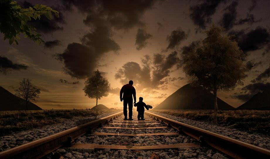 A father holding his son's hand walks in the sunset.