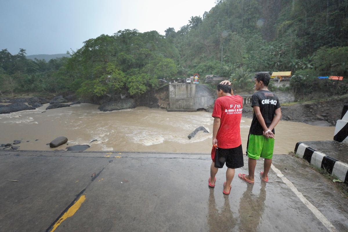 The day after Typhoon Bopha in 2012 raged through the southern Philippines island of Mindanao, two Filipinos view where a bridge once spanned the Cagayan River at Uguiaban. The floodwaters washed away the bridge, a vital part of a main highway through the region. A small footbridge remains. 