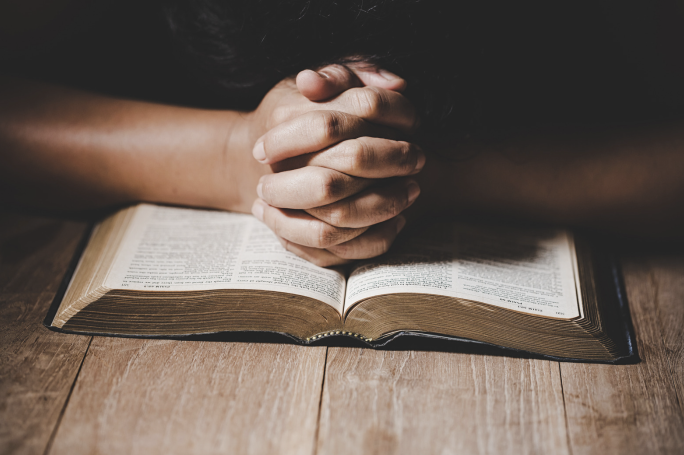 A man is praying with his hands on an open Bible.