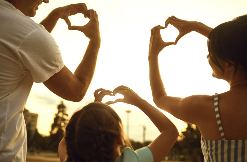 A picture of a family of three posting love gesture to each other