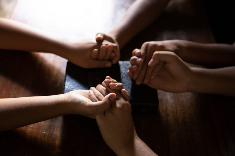 Several people hold hands and pray together.