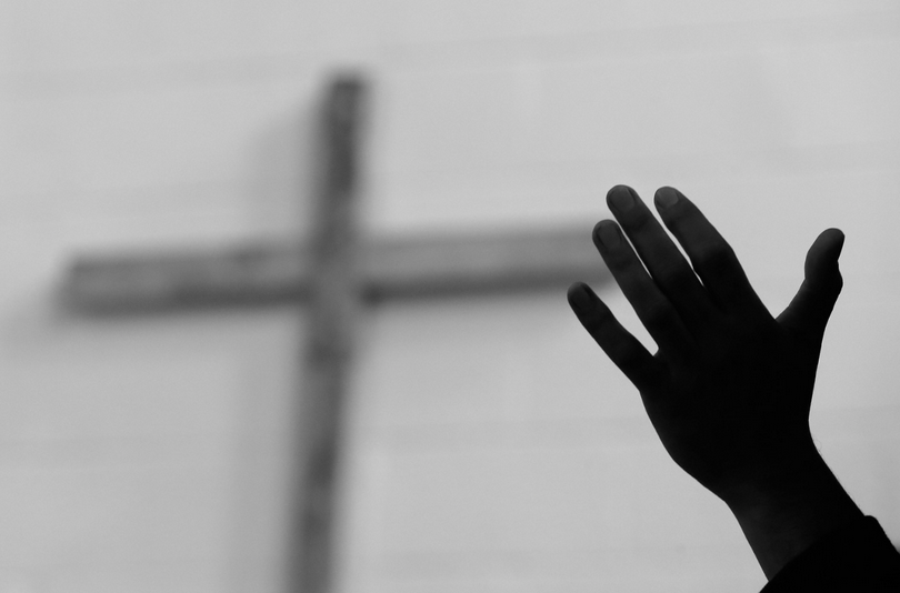 A hand is raised in front of the cross.