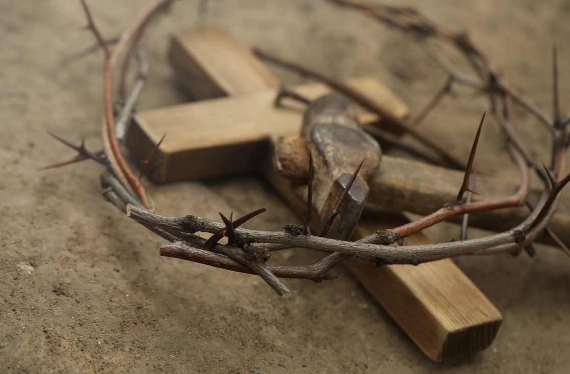 A closeup picture of crown of thorns, wooden cross and hammer on ground