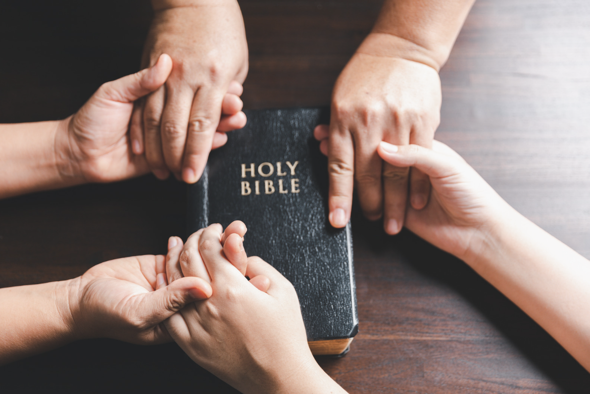 A picture of hands holding together on a Bible