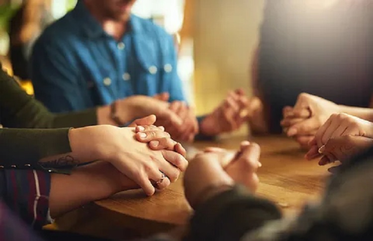 A picture of several persons holding hands to pray