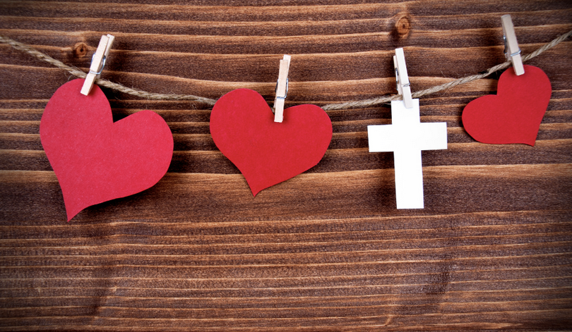 A picture of several hearts and a cross hanging on a wooden background.