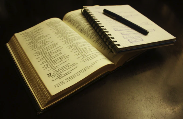 A notebook with a pen is placed on an open Bible on the desk.