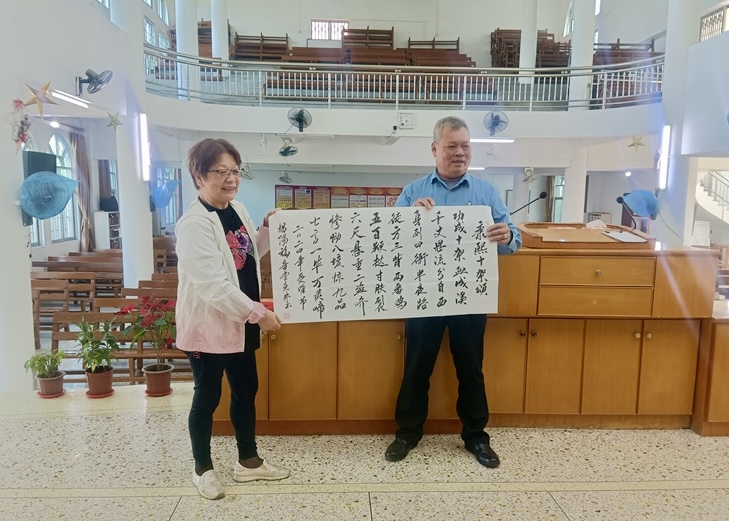 Mr. Yi Lin (right) shows the “Ode to the Cross” he copied with a brush.