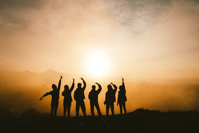 A picture of the silhouette of a group of people cheering towards the sun