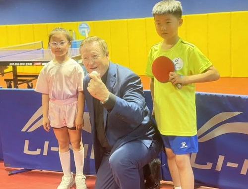 Dr. Gene Wood, founder and president of Word4Asia Consulting International, posed for a photo with two young table tennis players at the Nanjing Olympic Sports Center in Jiangsu during his visit to Nanjing from May 15 to 19, 2024, to discuss hosting the 5th Amity Cup International Table Tennis Philanthropic Tournament.