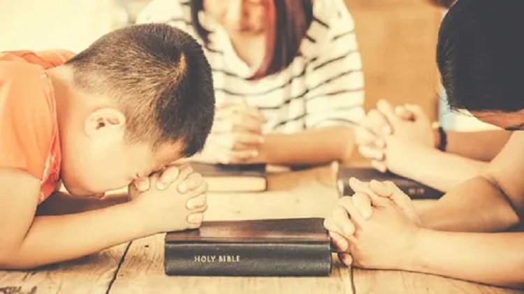 A picture of several children praying on the Bible