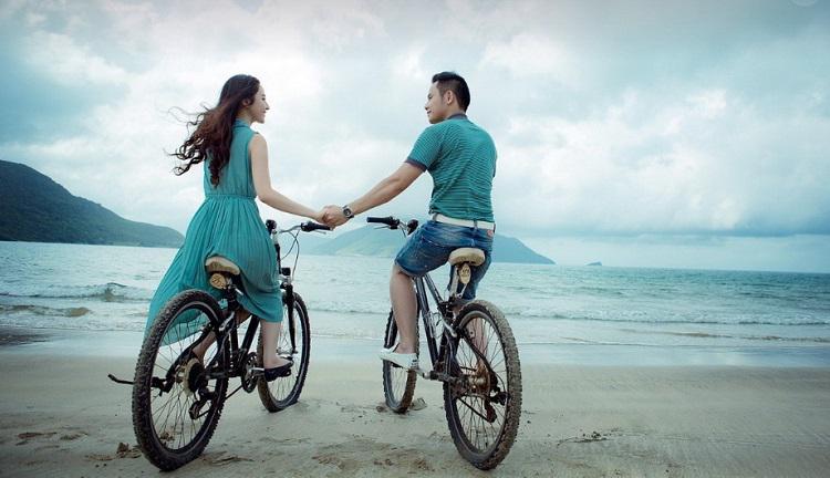 A picture of a woman and a man riding bicycles beside the sea