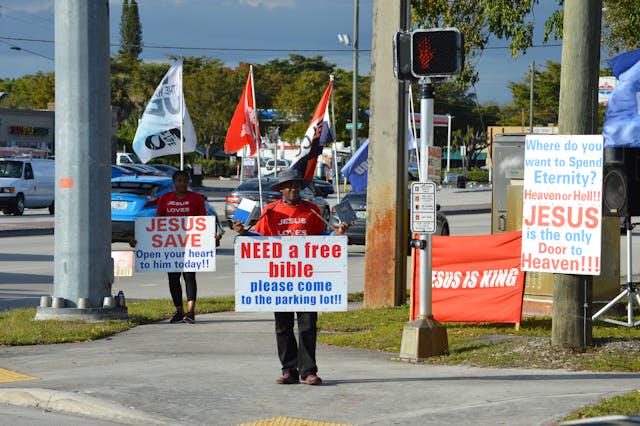 Men hold signs of "free bible" and "JESUS SAVE"