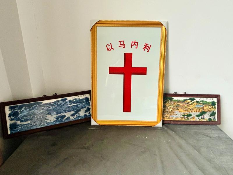 A porcelain cross stands beside both black-and-white and color versions of the famous Along the River During the Qingming Festival painting at Jingdezhen Church, in Jingdezhen City, Jiangxi Province.