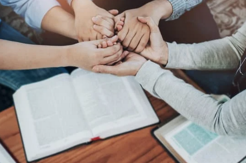 People pray together on top of open bibles.