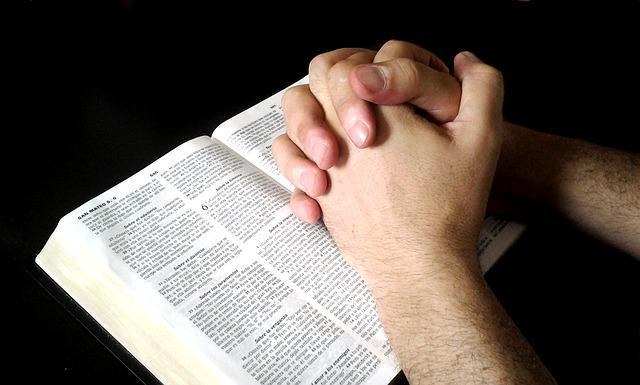 A man prays with his hands on the Bible.