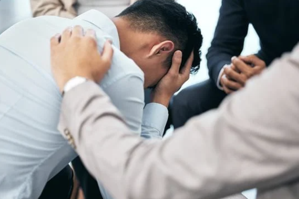 A supporting hand comforts a man suffering from mental health.