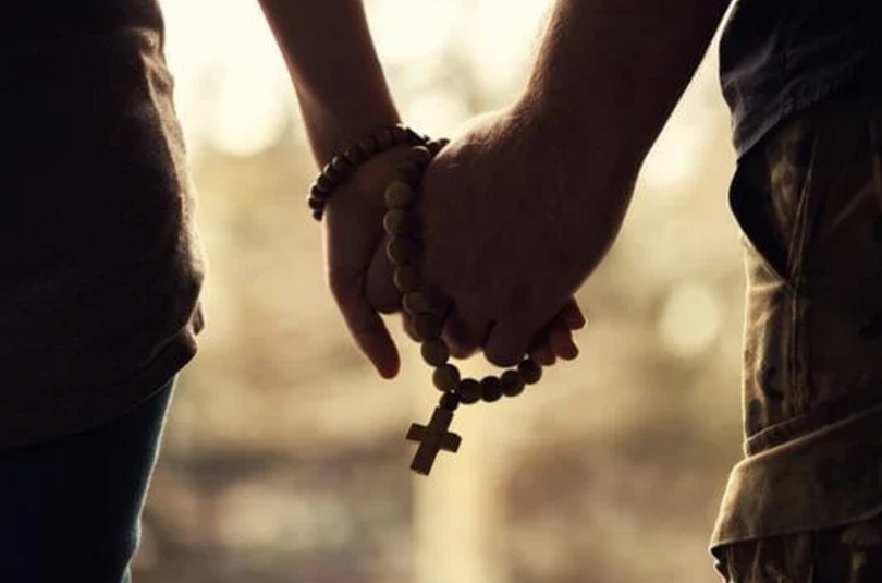 A couple together hold a cross in their hands.