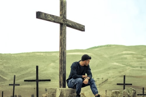 A man sits under a cross.
