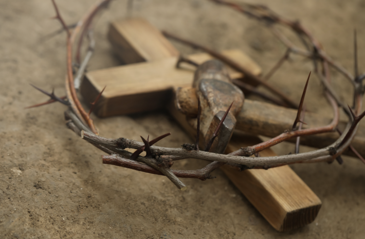 A closeup picture of crown of thorns, wooden cross and hammer on ground