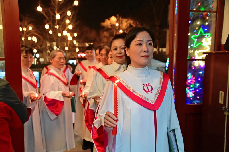 Christians in robes holding candles processed through the church doors at a church in Beijing during Christmas Week 2024.