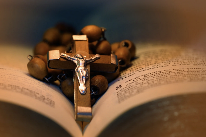 A wooden crucifix with a metal figure of Jesus Christ was placed on an open Bible with a set of wooden rosary beads surrounding the crucifix.