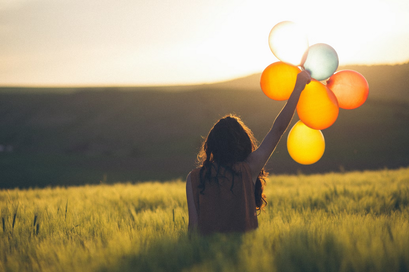 An unknown woman holds balloons outdoors.