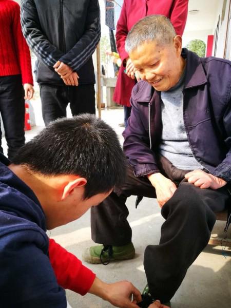 A volunteer puts the shoes on a leprosy survivor 