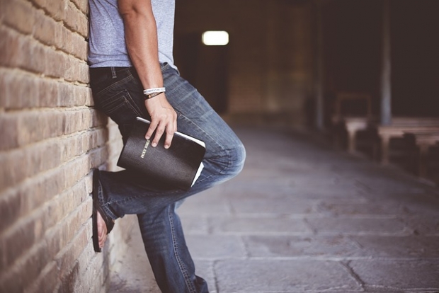 A man leans on a wall, holding a Bible in his hand