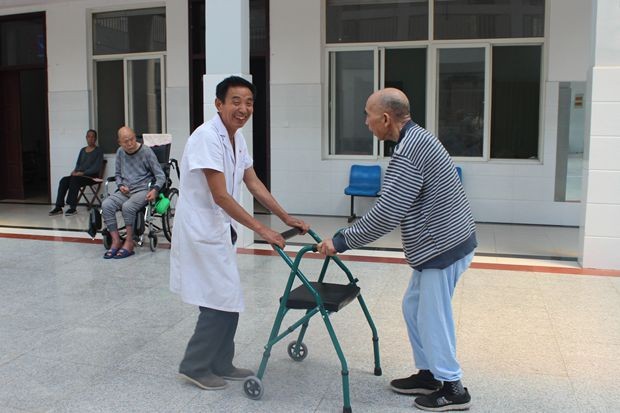  Inside the home: a male nurse assists an elderly man to work out with the help of a senior walking aid 