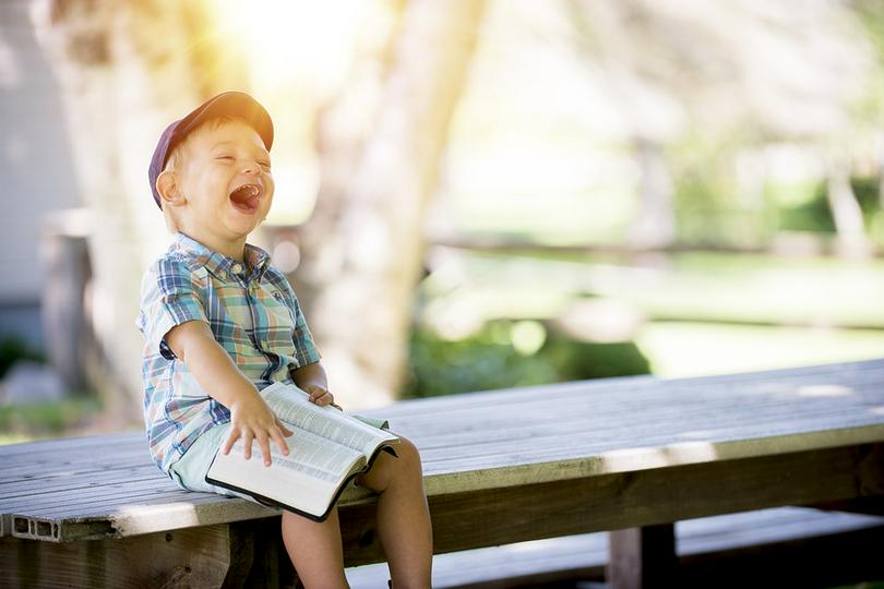 A boy laughs while reading a book.