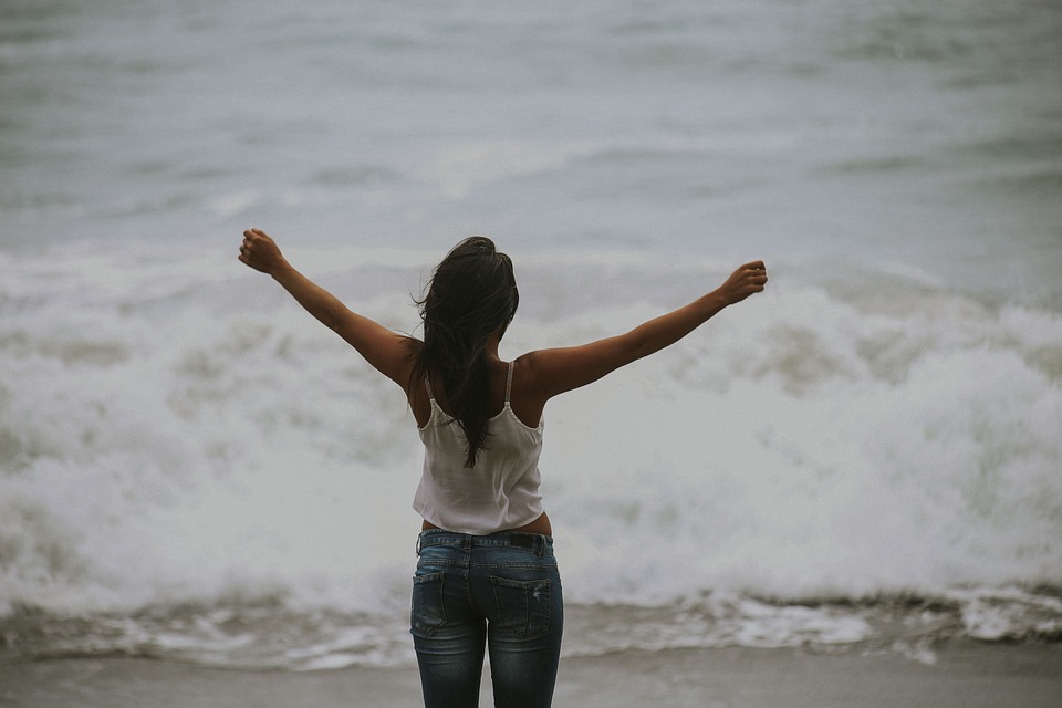 A woman stands by the sea with opening arms. 
