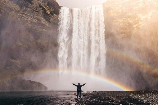 A man raises his own before a waterfall.