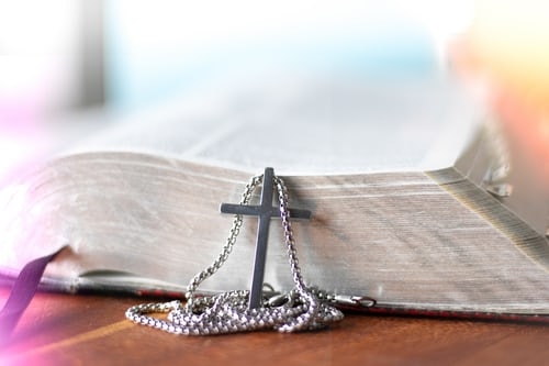 A cross necklace lays behind the Bible. 