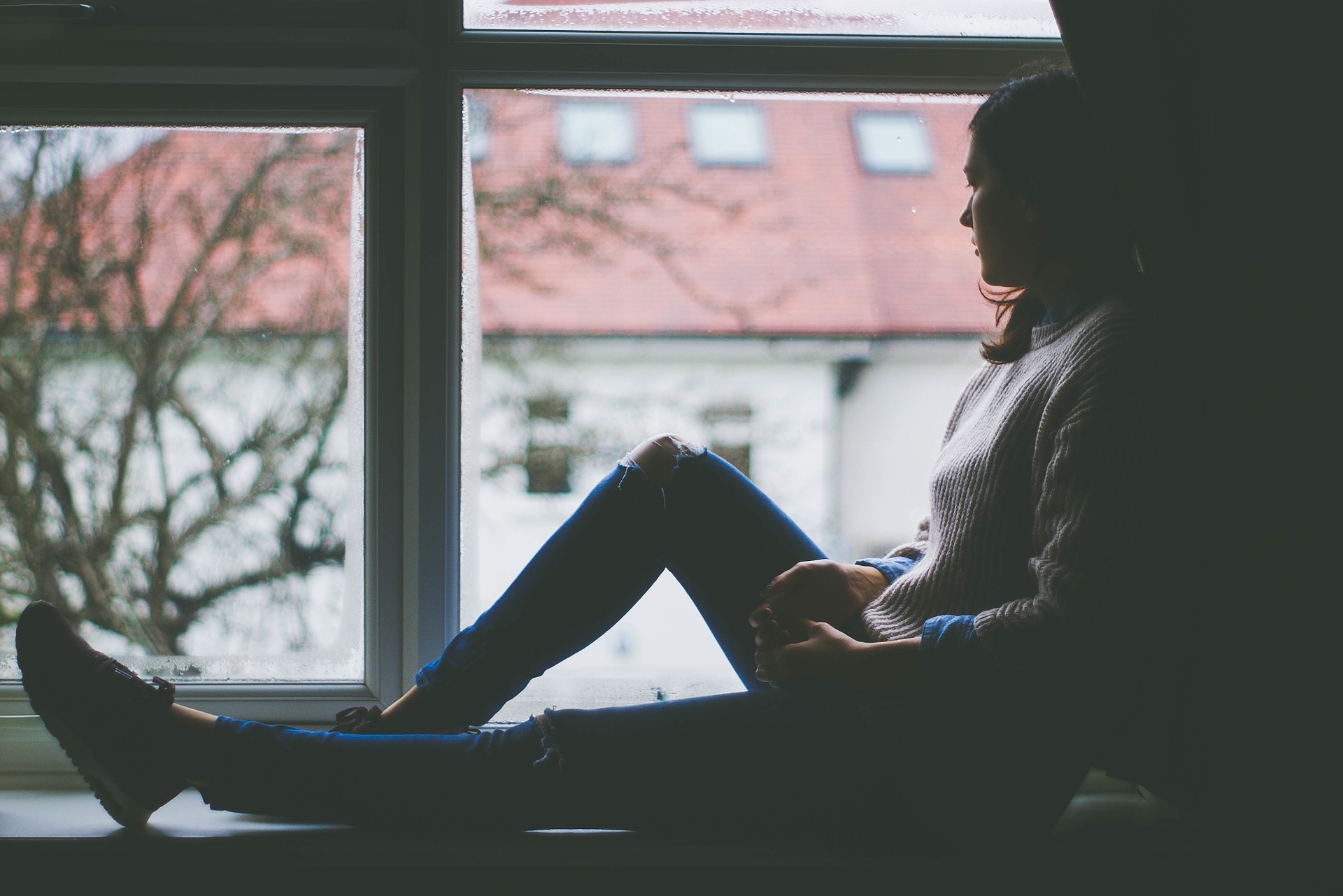 A woman sits beside a window. 