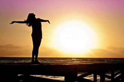 A woman opens her arms in front of the sea.