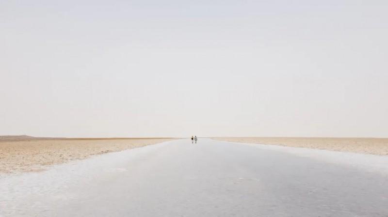 Two men walk on an empty road.