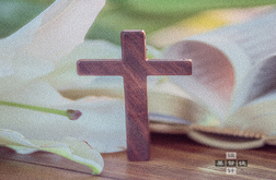 A cross lays besides a lily and the Bible. 
