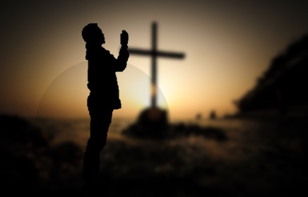 A man prays besides a cross.