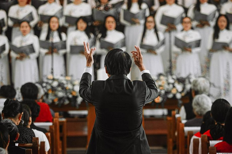 A picture shows a conductor leading a choir in singing a hymn in a church.