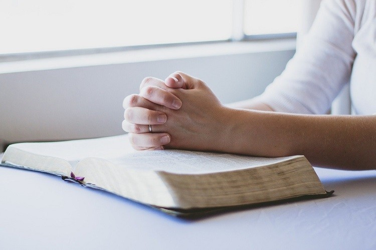 A picture shows a person praying with hands folded.