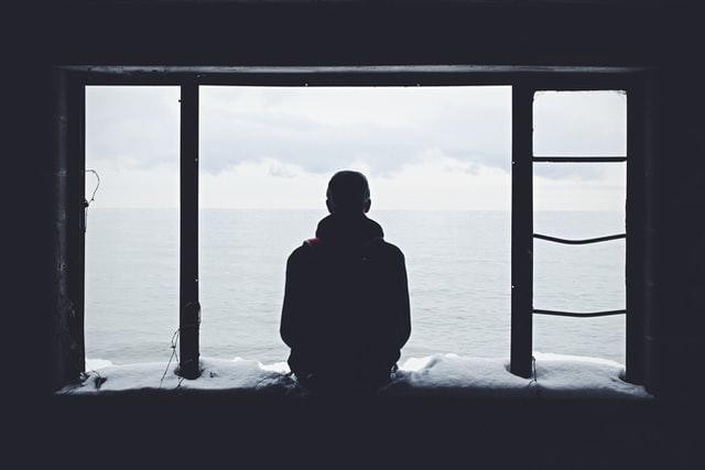 A picture shows a man sitting on a windowsill on a snowy day.