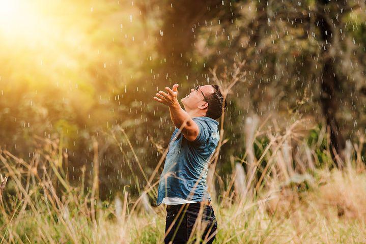 A picture shows a man embracing the rain with open arms.