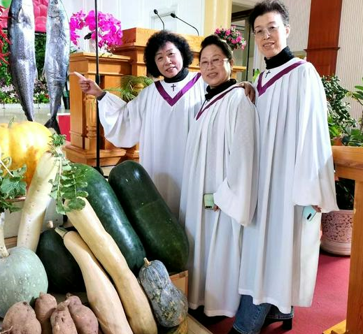 Three choir members took a group picture besides big fish and vegetables after a Sunday service to celebrate the Autumn Harvest Festival in Shuishiying Church, Dalian, Liaoning, on October 16, 2022.