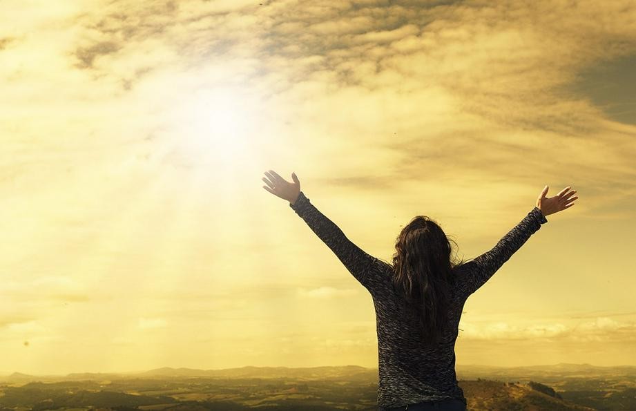 A picture shows a woman stretching her arms towards the sun.